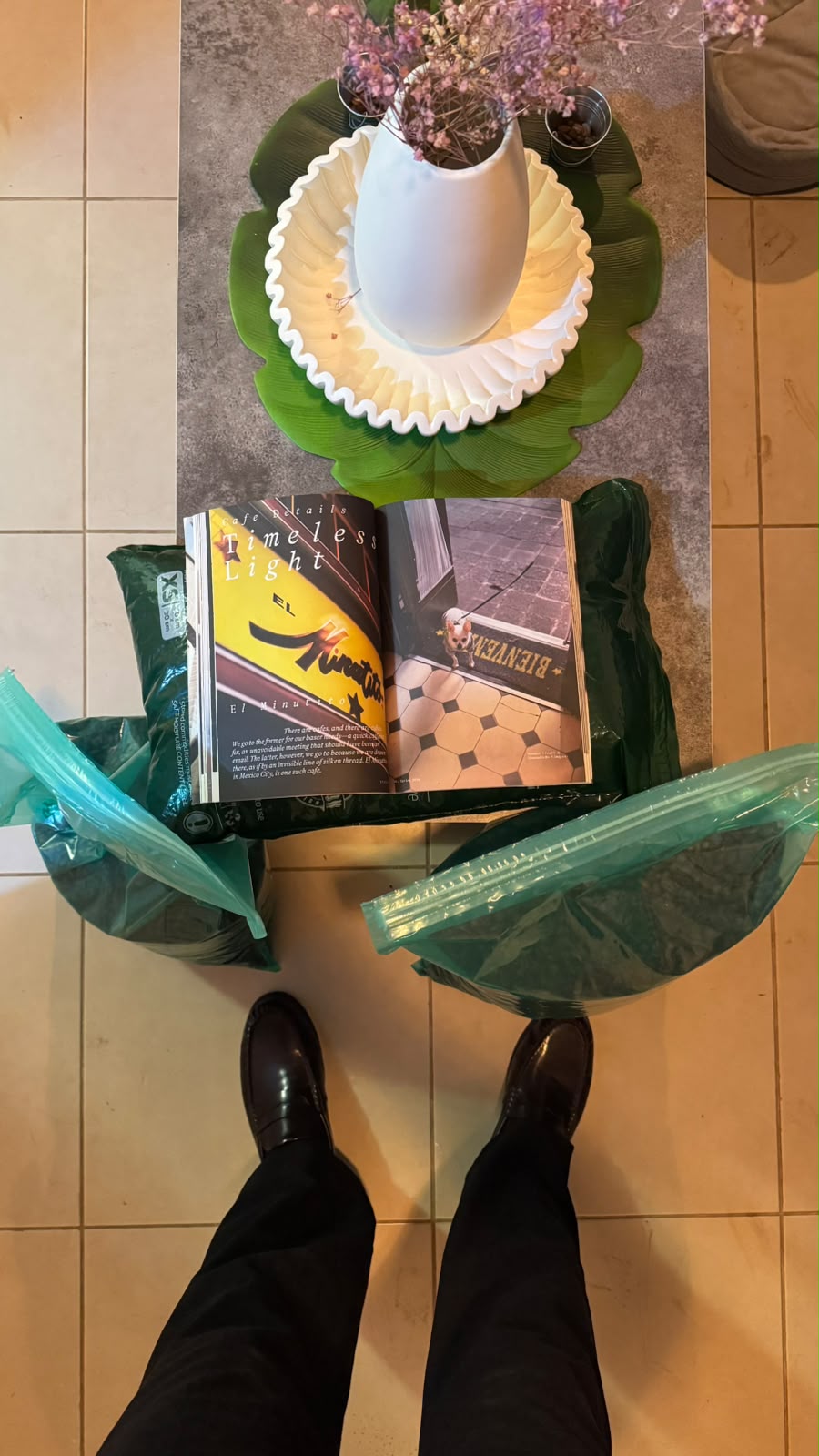 Una revista abierta junto a flores y bolsas de café, vista desde arriba
